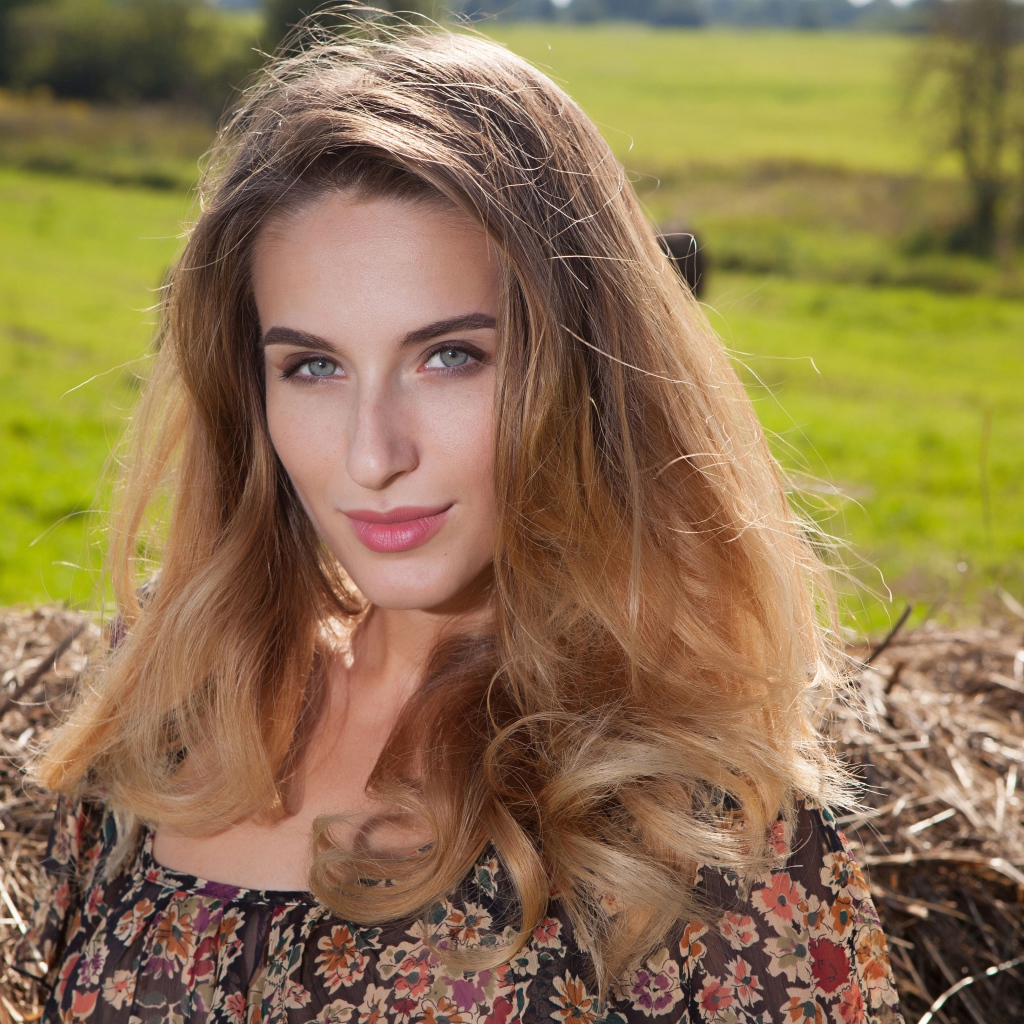 Красивая девушка с серыми глазами стоит у сена