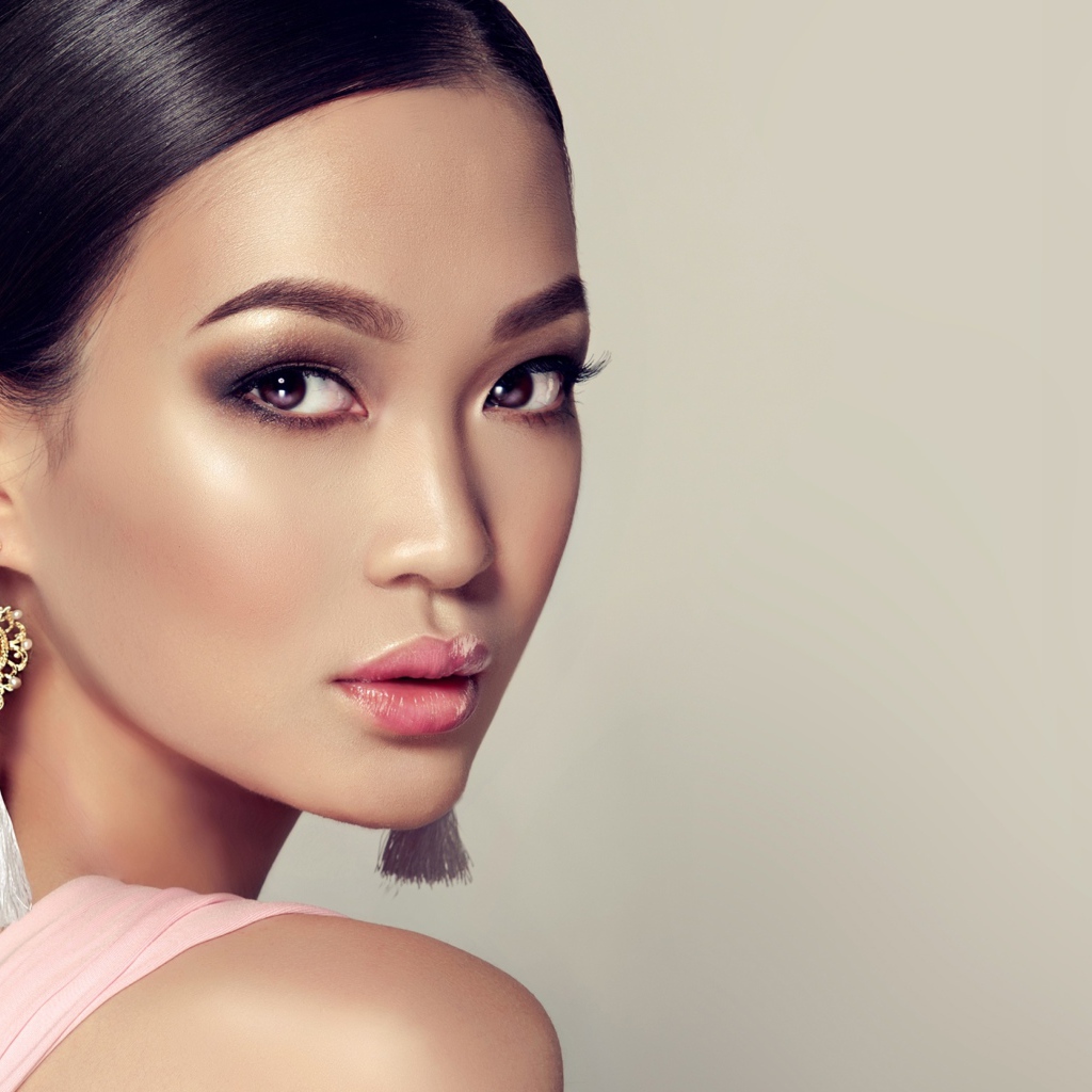 Красивая девушка с прической и сережками в ушах на сером фоне