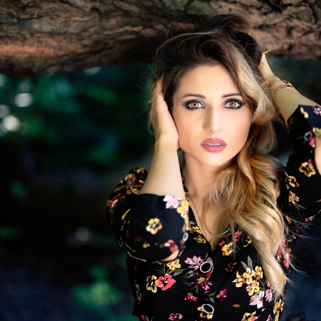 Красивая девушка с руками в волосах у дерева