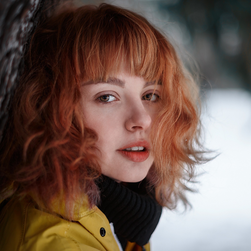 Красивая рыжеволосая девушка стоит у дерева зимой