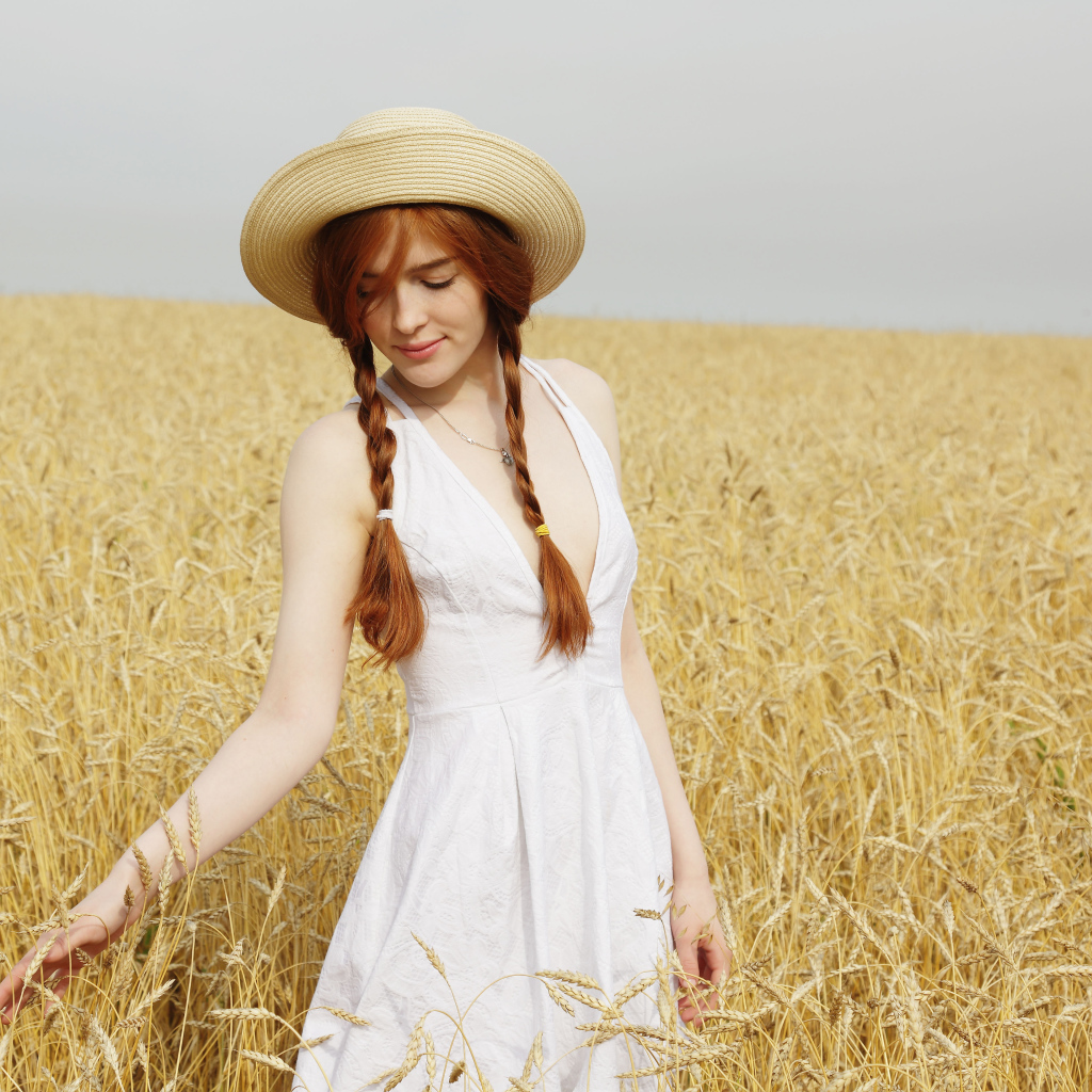 Красивая рыжеволосая девушка гуляет по полю с пшеницей