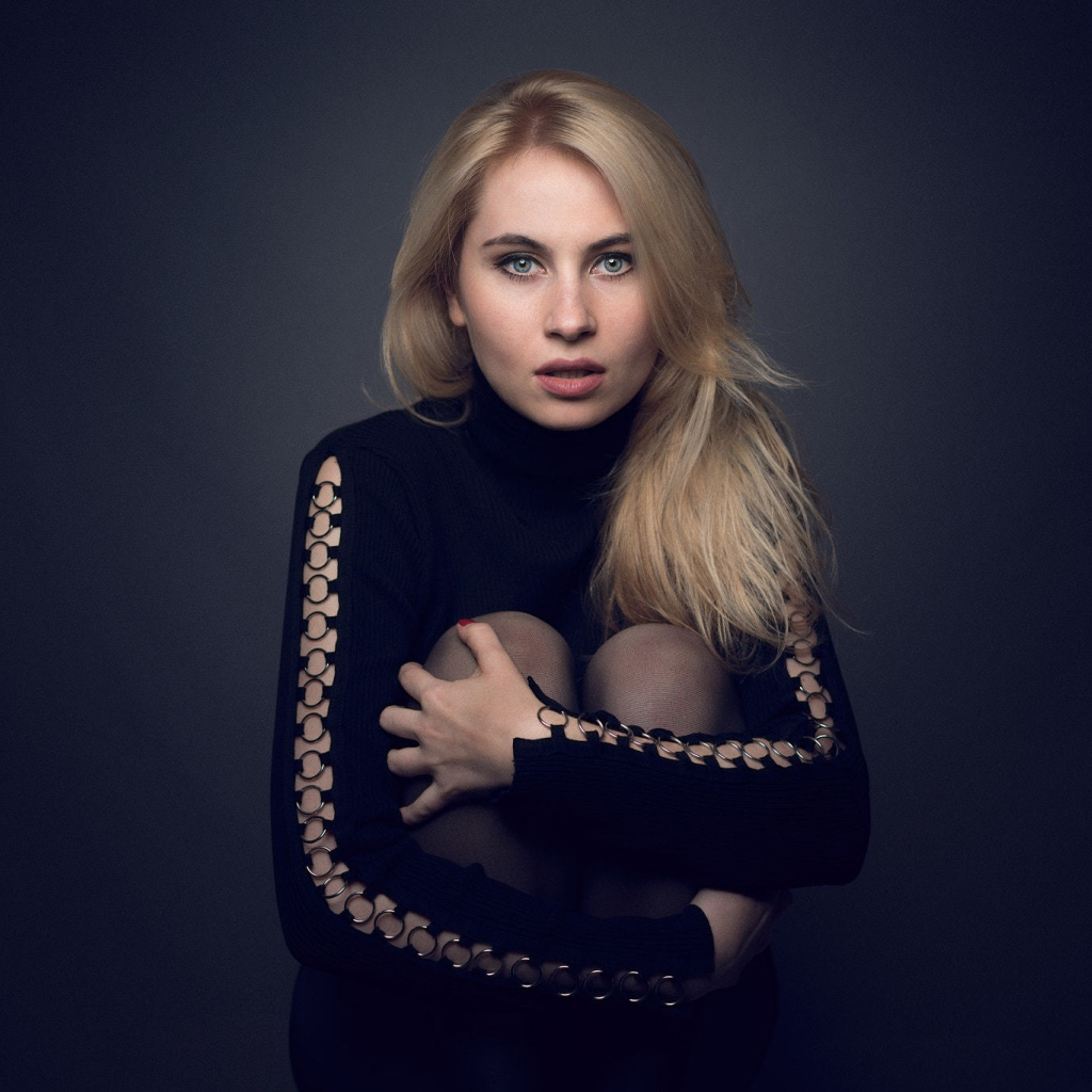 Блондинка в черном наряде на сером фоне