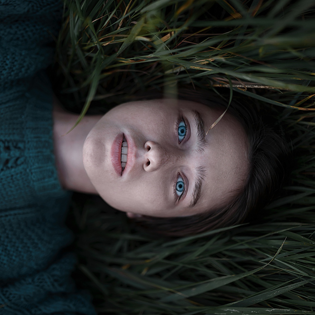 Голубоглазая девушка в свитере лежит на траве