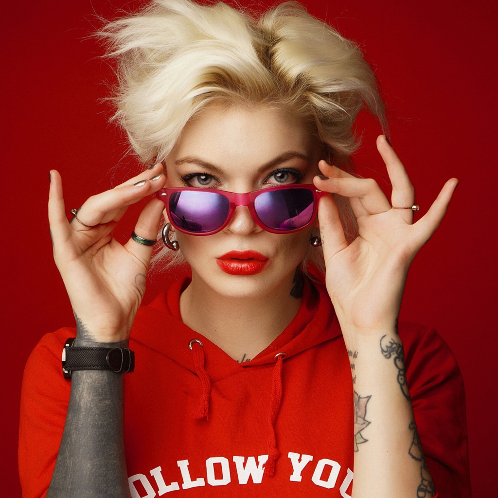 Яркая блондинка с татуировками на руках на красном фоне