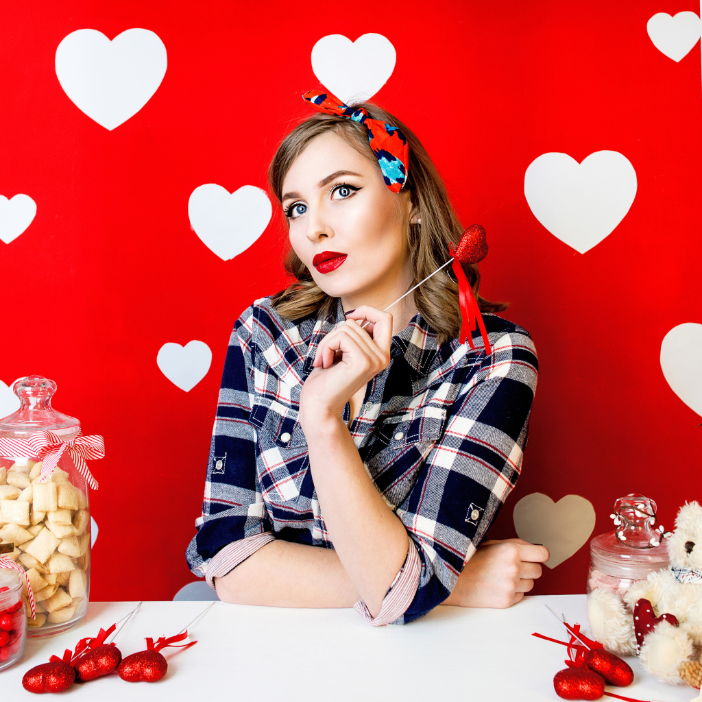 Яркая девушка за столом со сладостями на красном фоне с белыми сердечками 