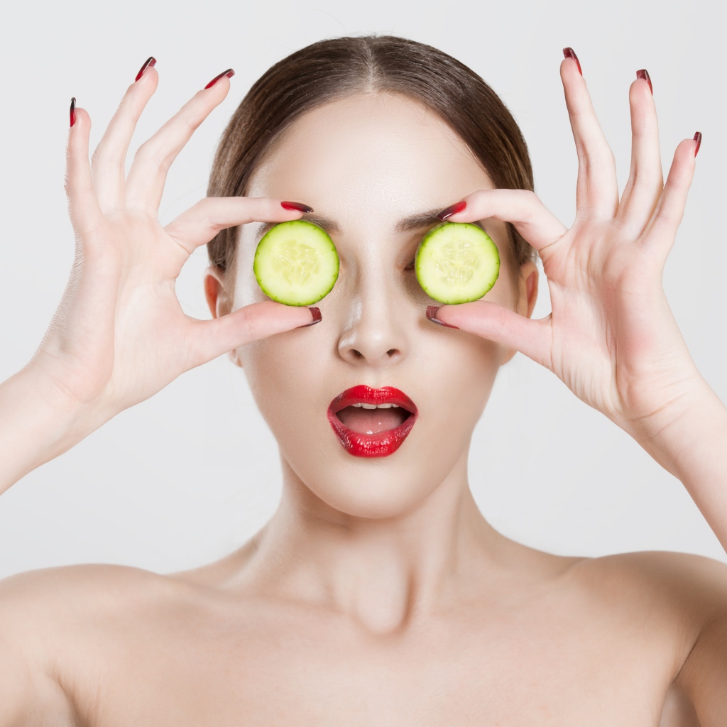 Яркая девушка с огурцами у глаз на сером фоне