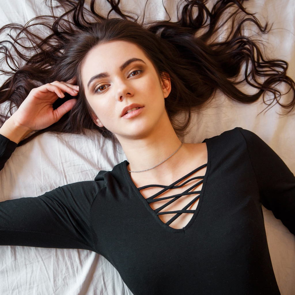 Кареглазая девушка в черном лежит на кровати