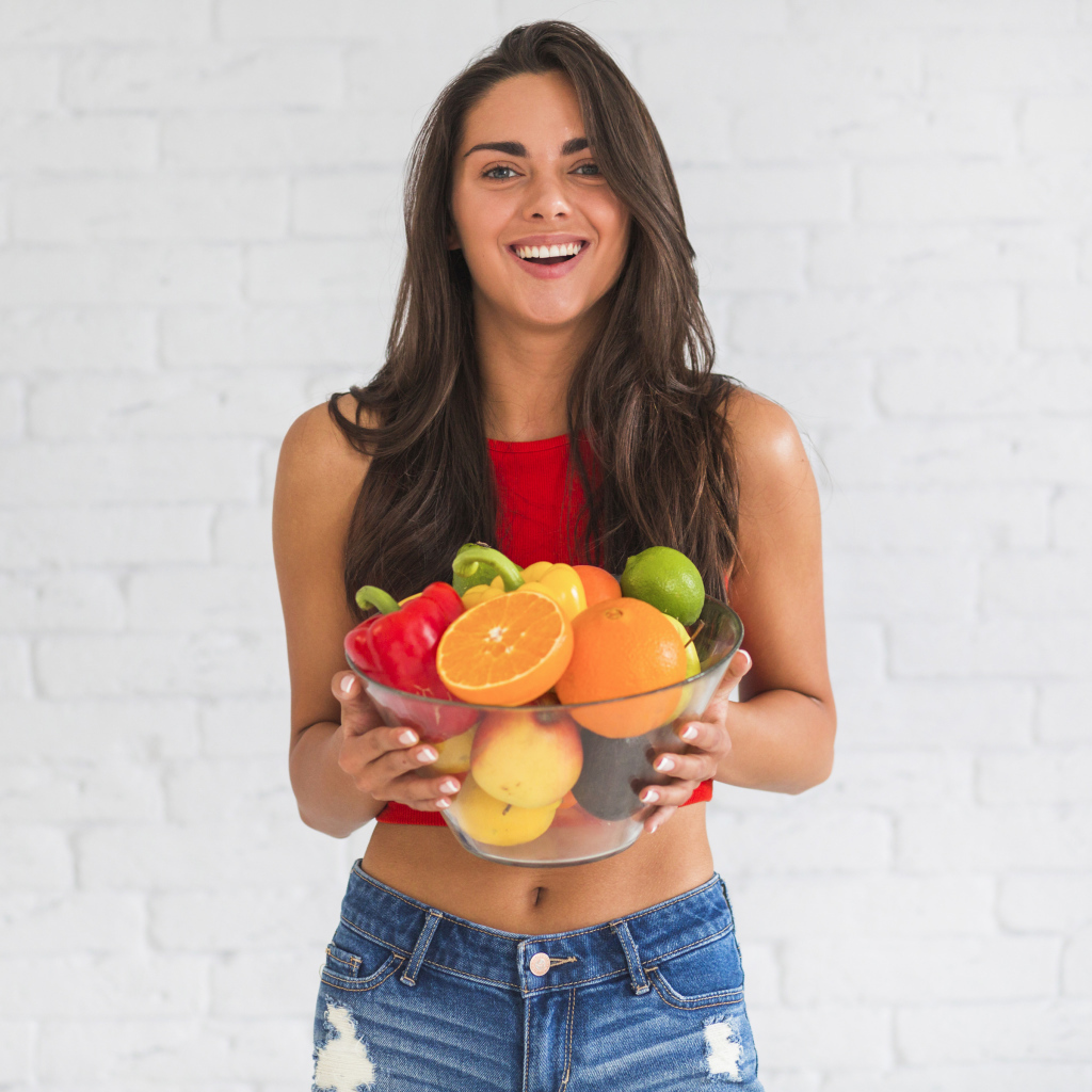Брюнетка с миской фруктов на фоне стены