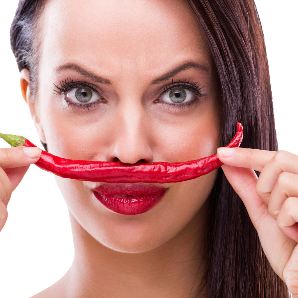 Брюнетка с красным перцем у лица на белом фоне