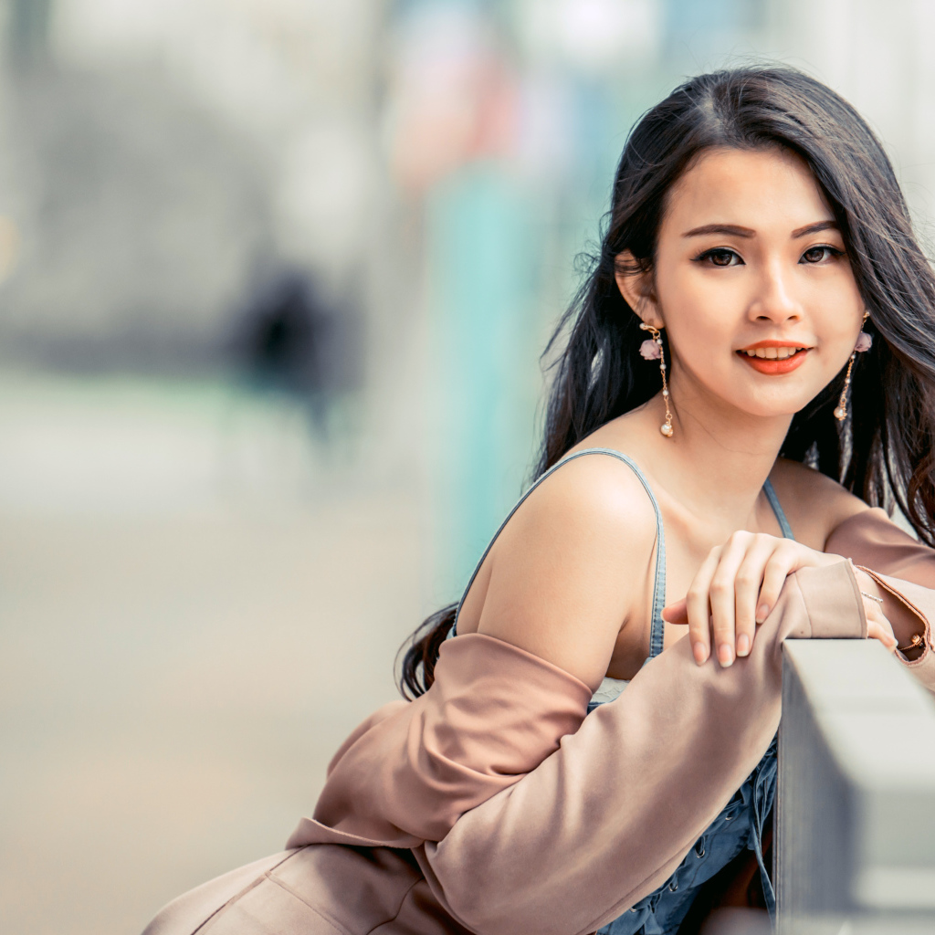 Очаровательная девушка азиатка сидит на лавке