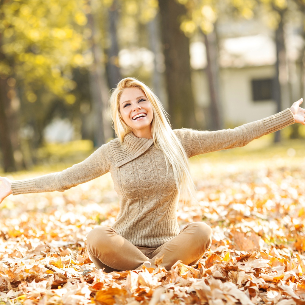 Веселая девушка сидит на опавшей листве осенью 