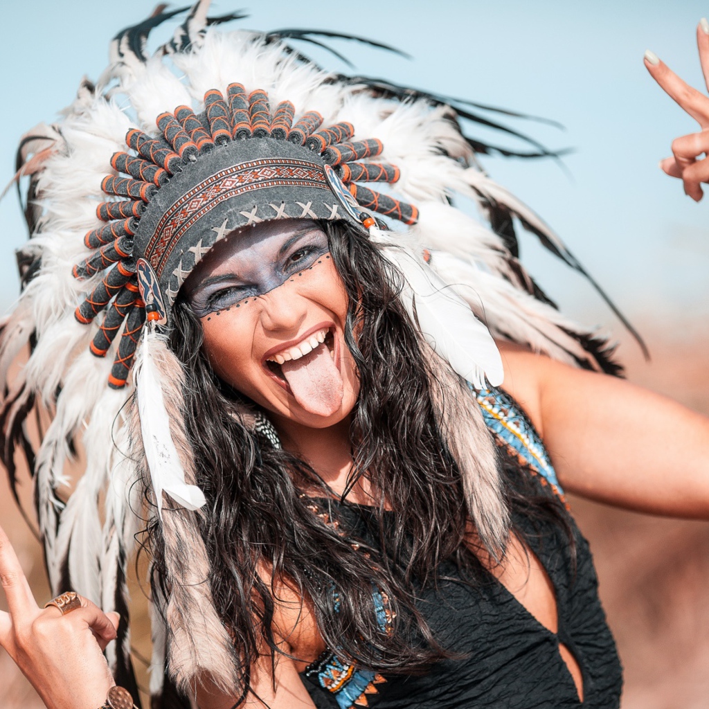 Веселая девушка с высунутым языком в костюме индейца
