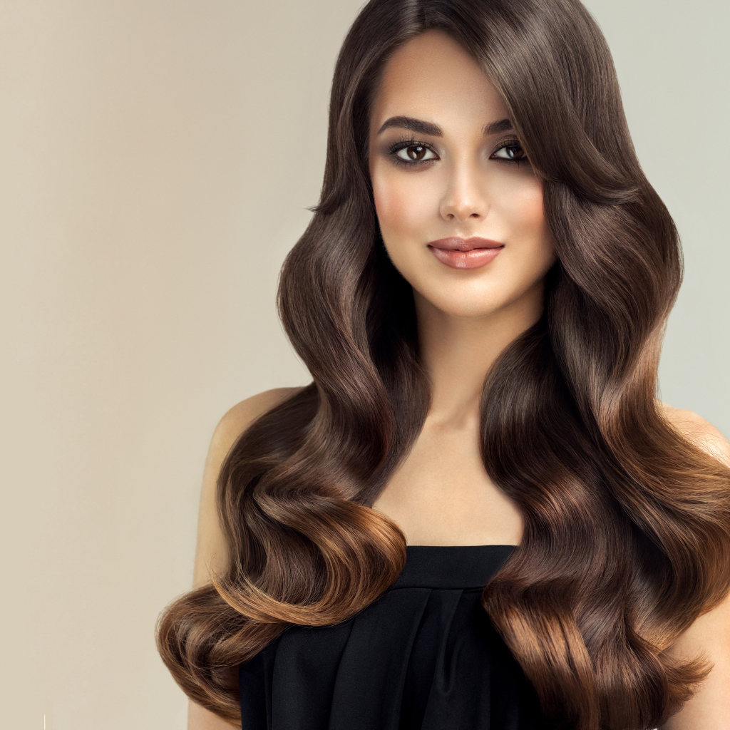 Милая кареглазая девушка с красивыми длинными волосами на сером фоне