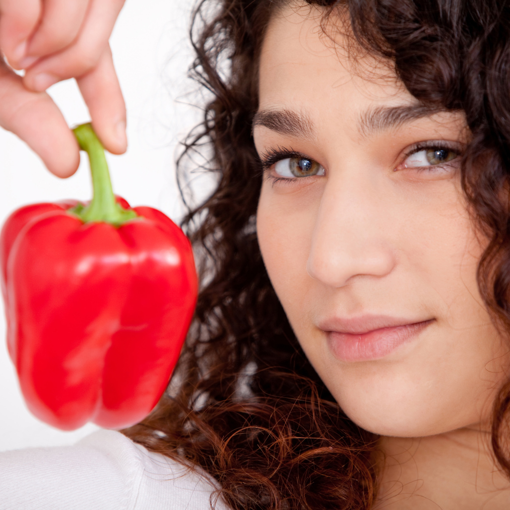Лицо девушки с красным сладким перцем в руке крупным планом