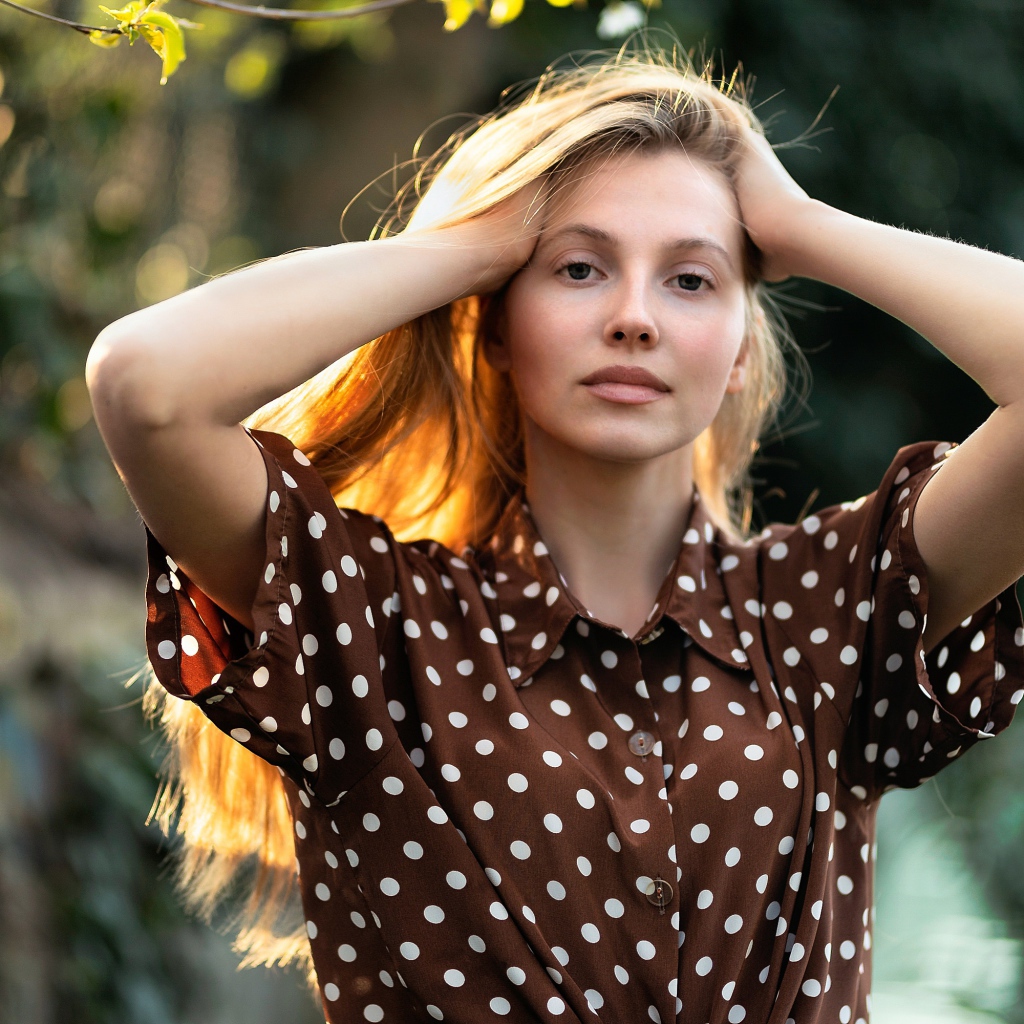 Девушка в рубашке в горох с руками в волосах 