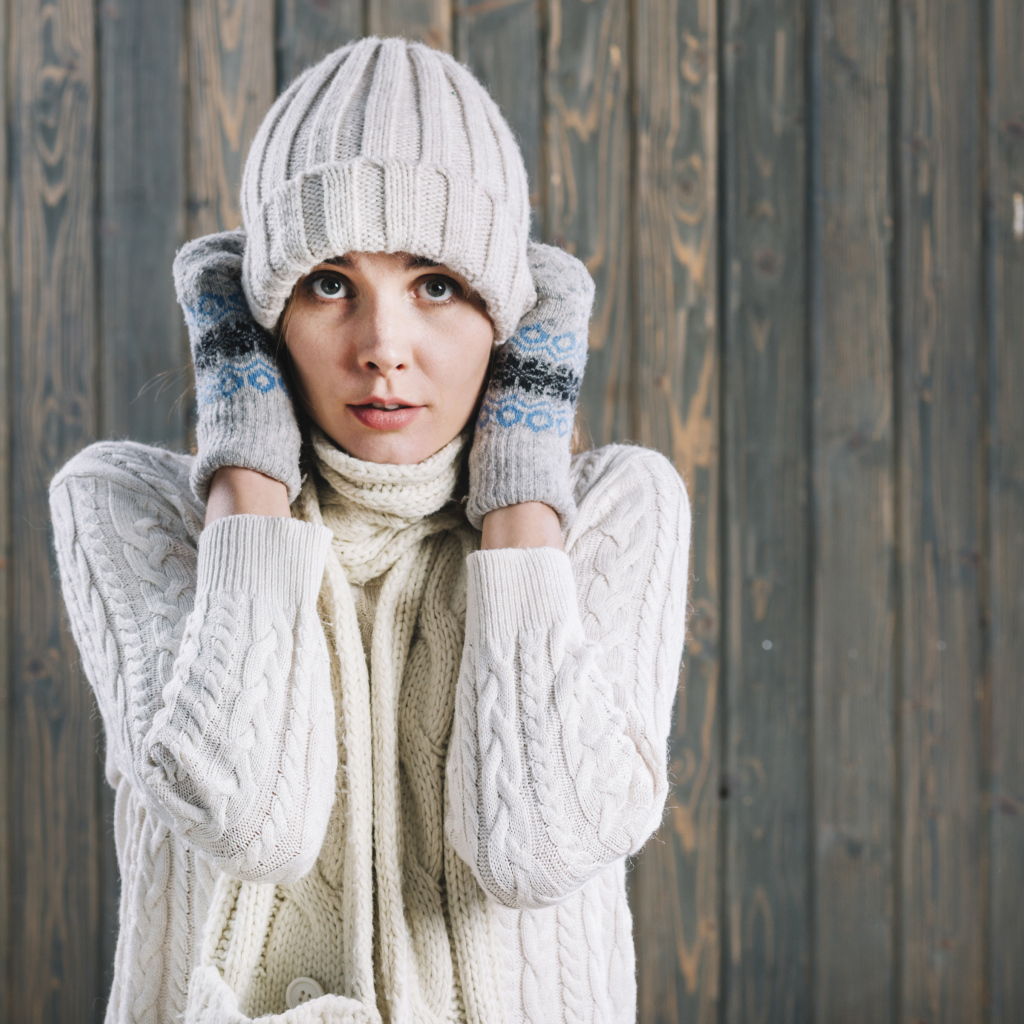 Девушка в варежках поправляет шапку на голове