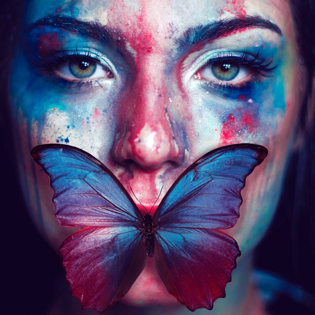 Лицо девушки в краске с бабочкой во рту
