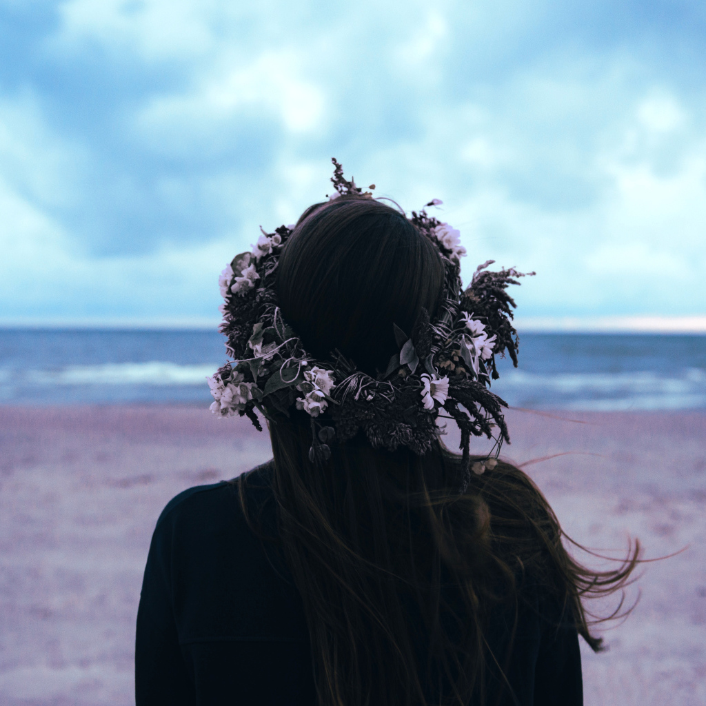 Девушка с венком на голове на фоне моря вид сзади