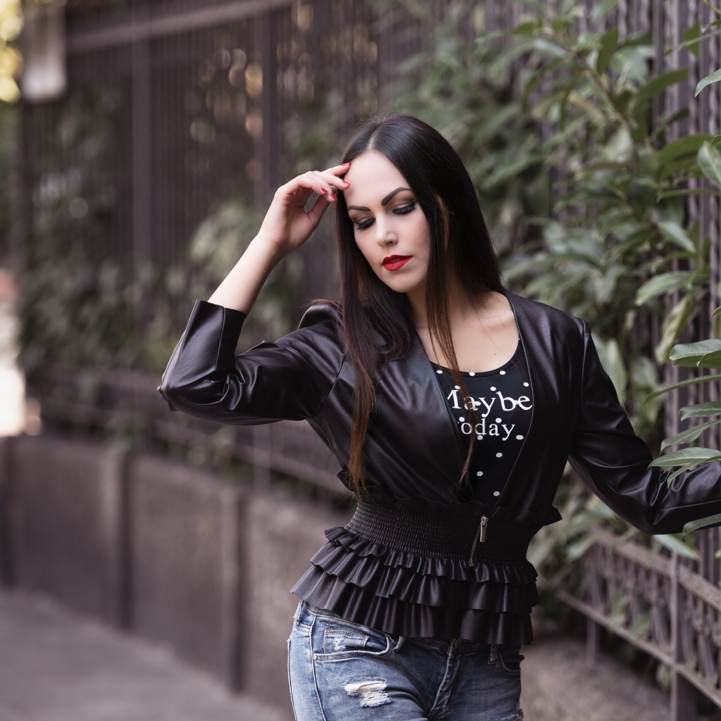 Длинноволосая брюнетка в черной куртке у забора