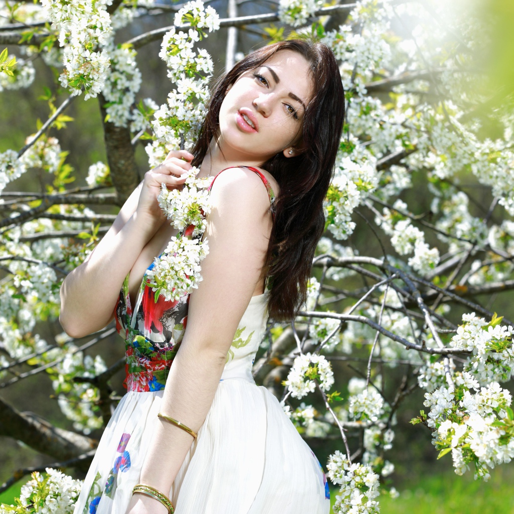 Длинноволосая девушка стоит у цветущей вишни 
