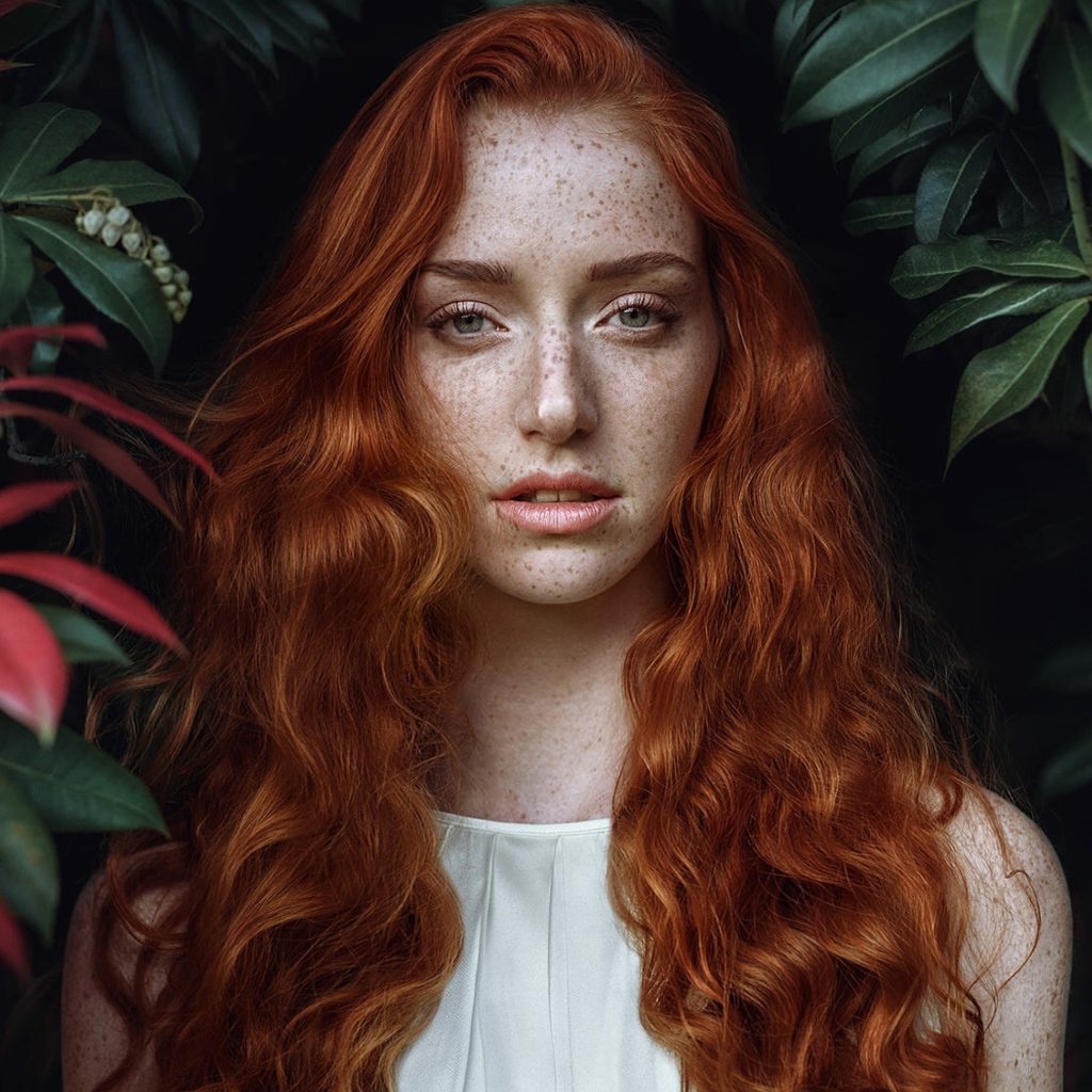 Рыжеволосая девушка с веснушками на лице на фоне кустов 