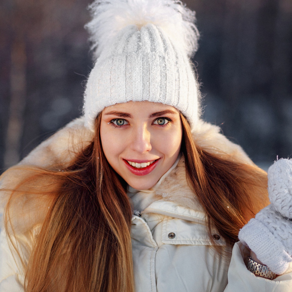 Улыбающаяся девушка в теплой шапке и варежках зимой
