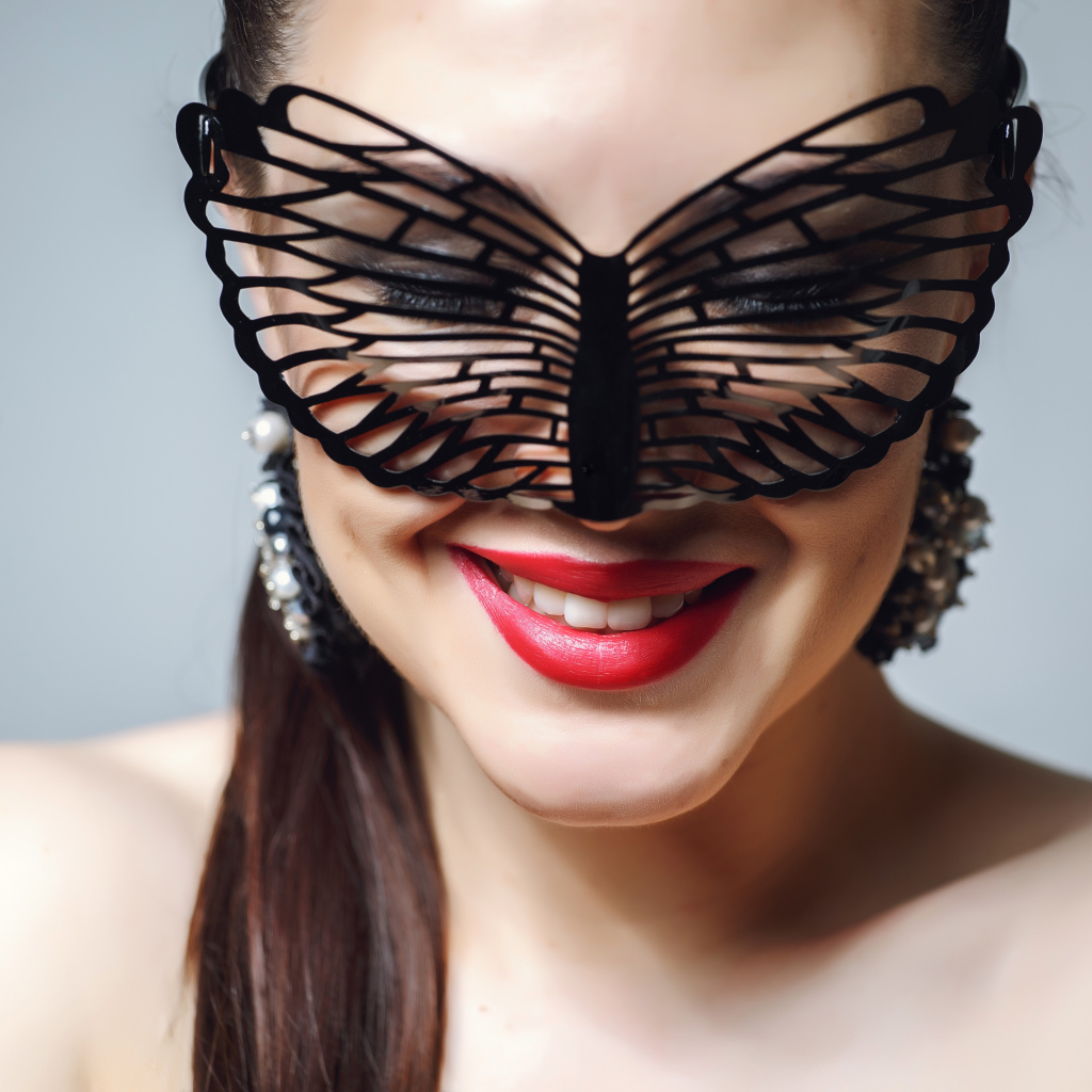 Улыбающаяся девушка в черной маске на сером фоне