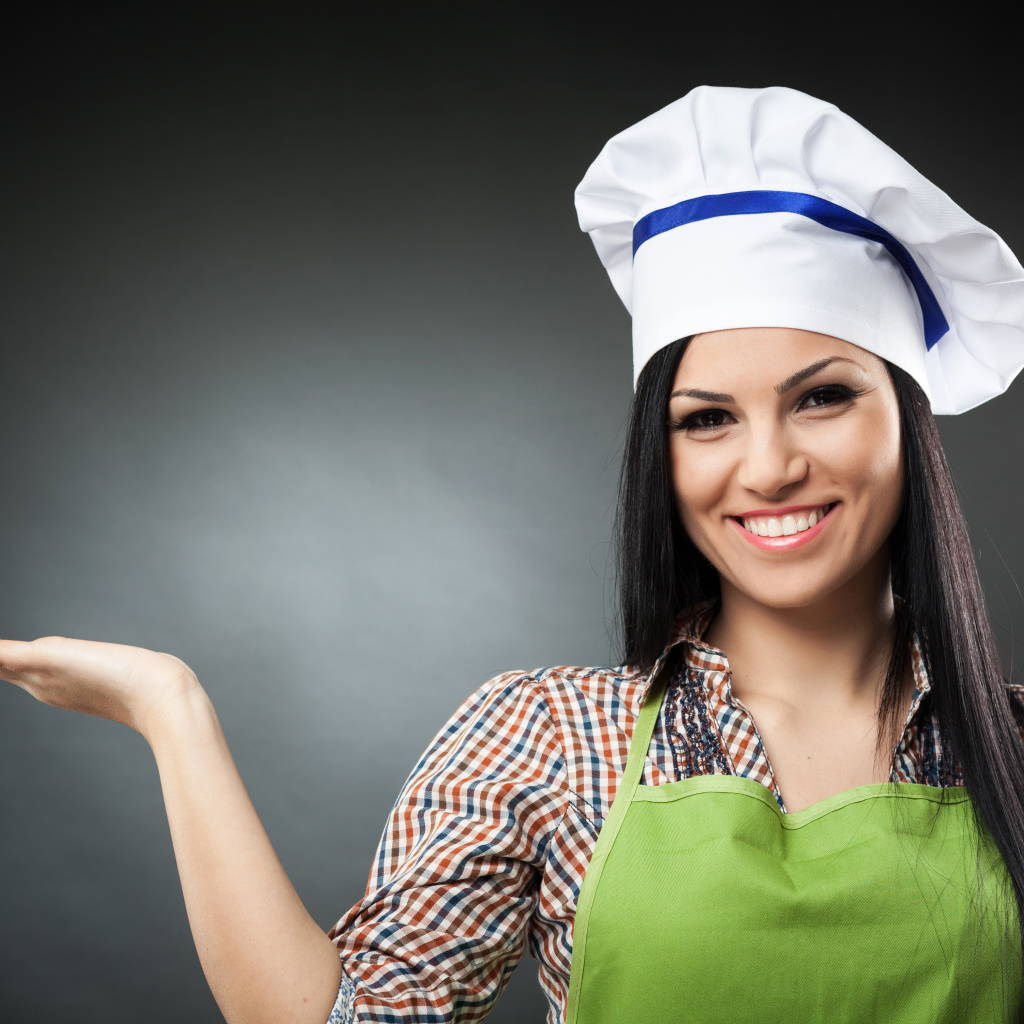 Улыбающаяся девушка в поварском колпаке на сером фоне