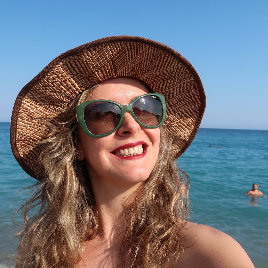 Улыбающаяся девушка в солнечных очках и шляпе на море