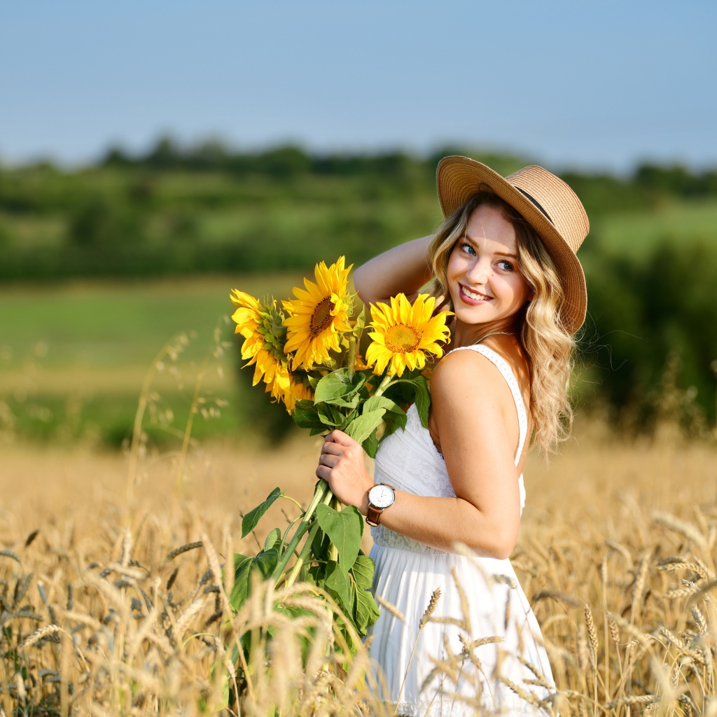 Улыбающаяся девушка на поле с пшеницей с букетом подсолнухов в руке