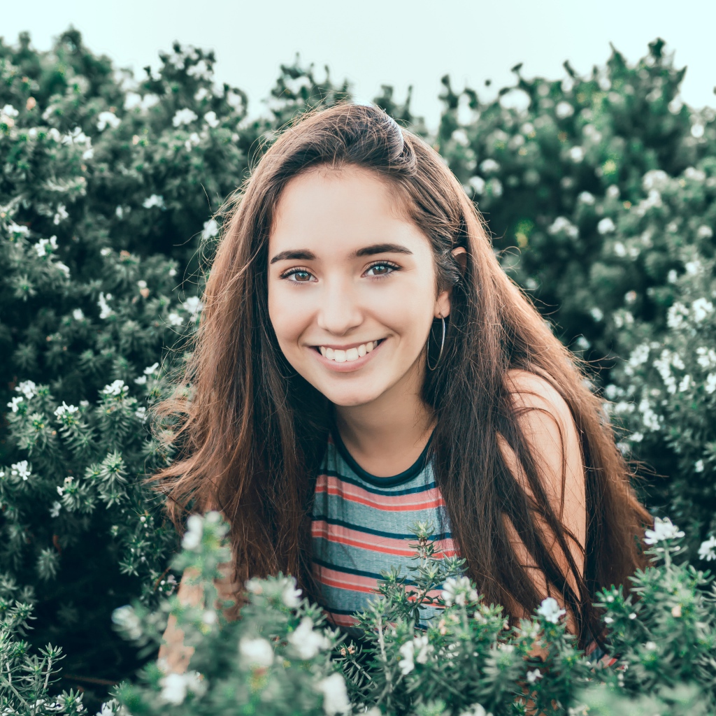 Улыбающаяся девушка сидит в зеленых зарослях 