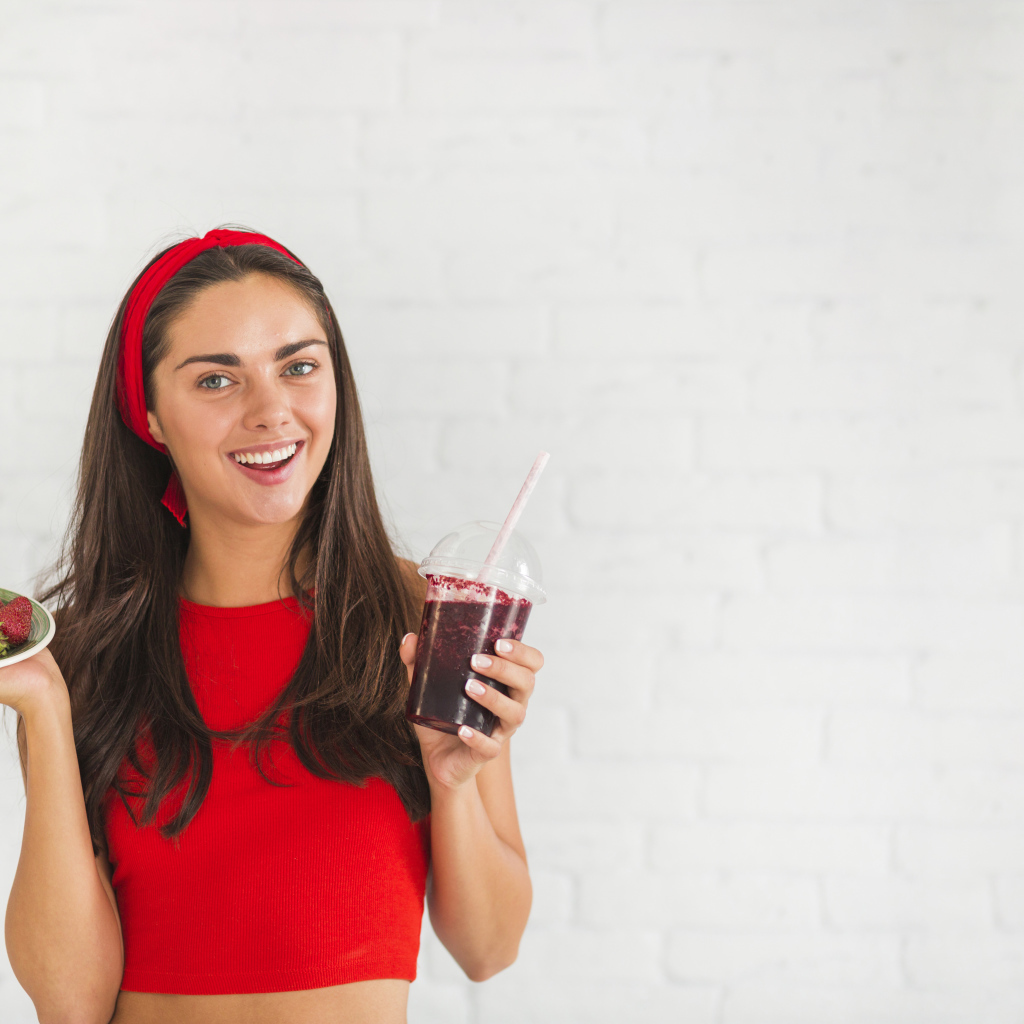 Улыбающаяся девушка с клубникой и смузи в руках
