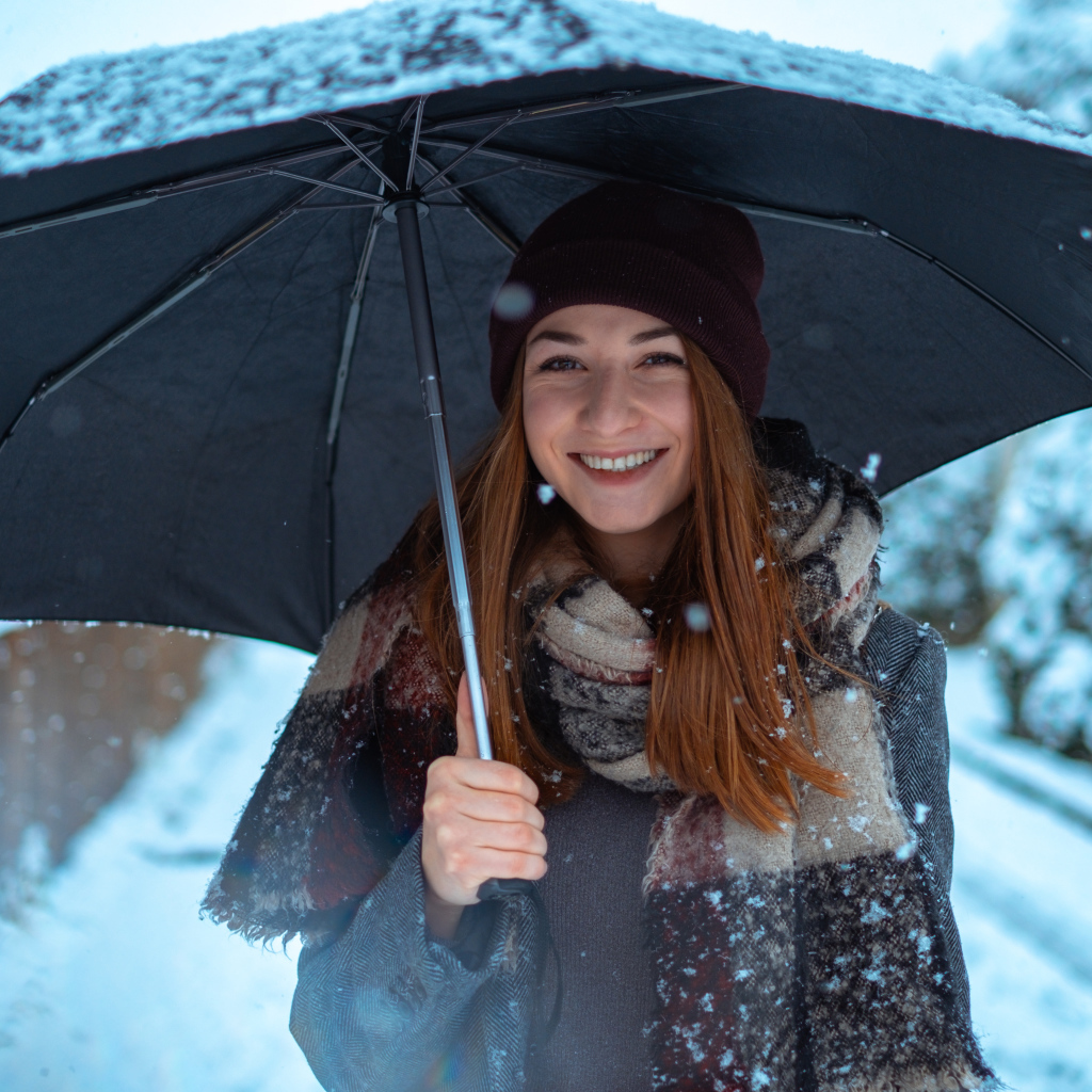 Улыбающаяся молодая девушка под зонтом зимой