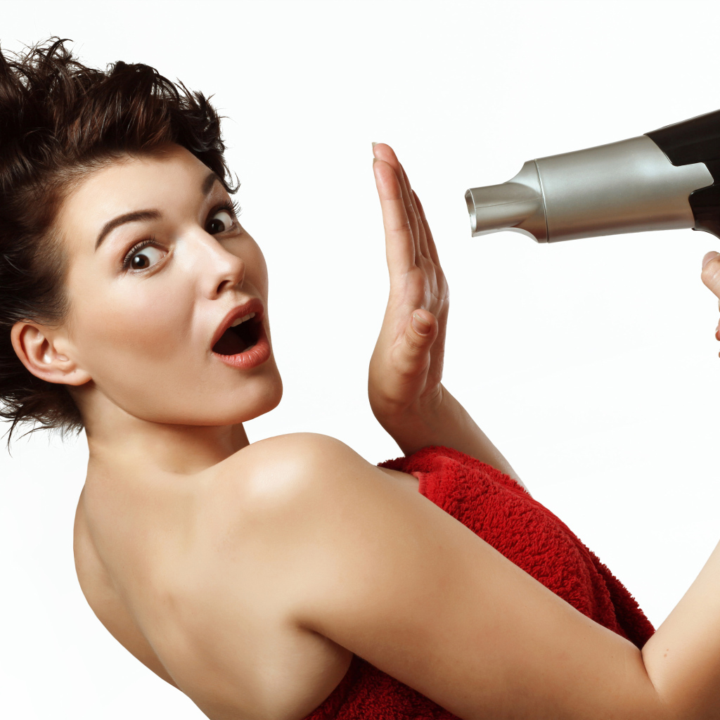 Удивленная девушка с феном в руках на белом фоне