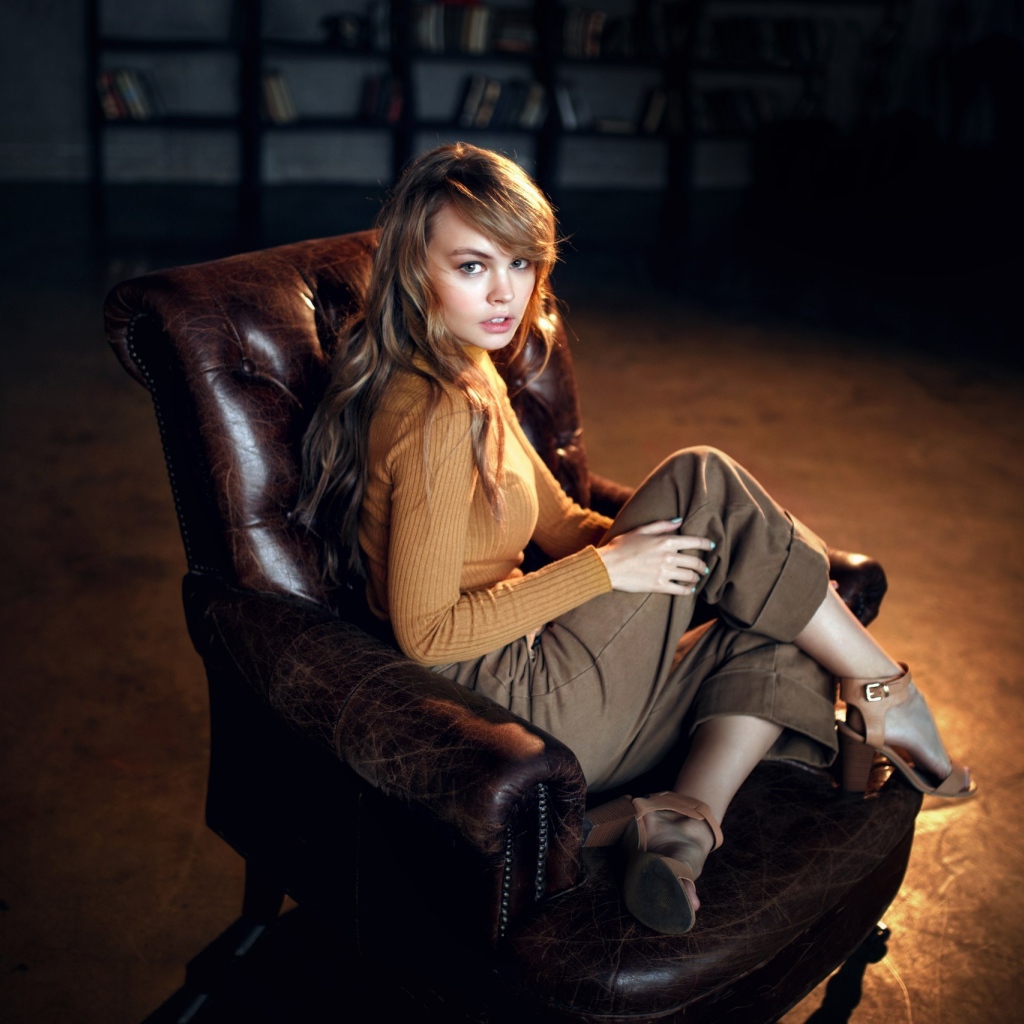 Нежная девушка модель сидит в кожаном кресле