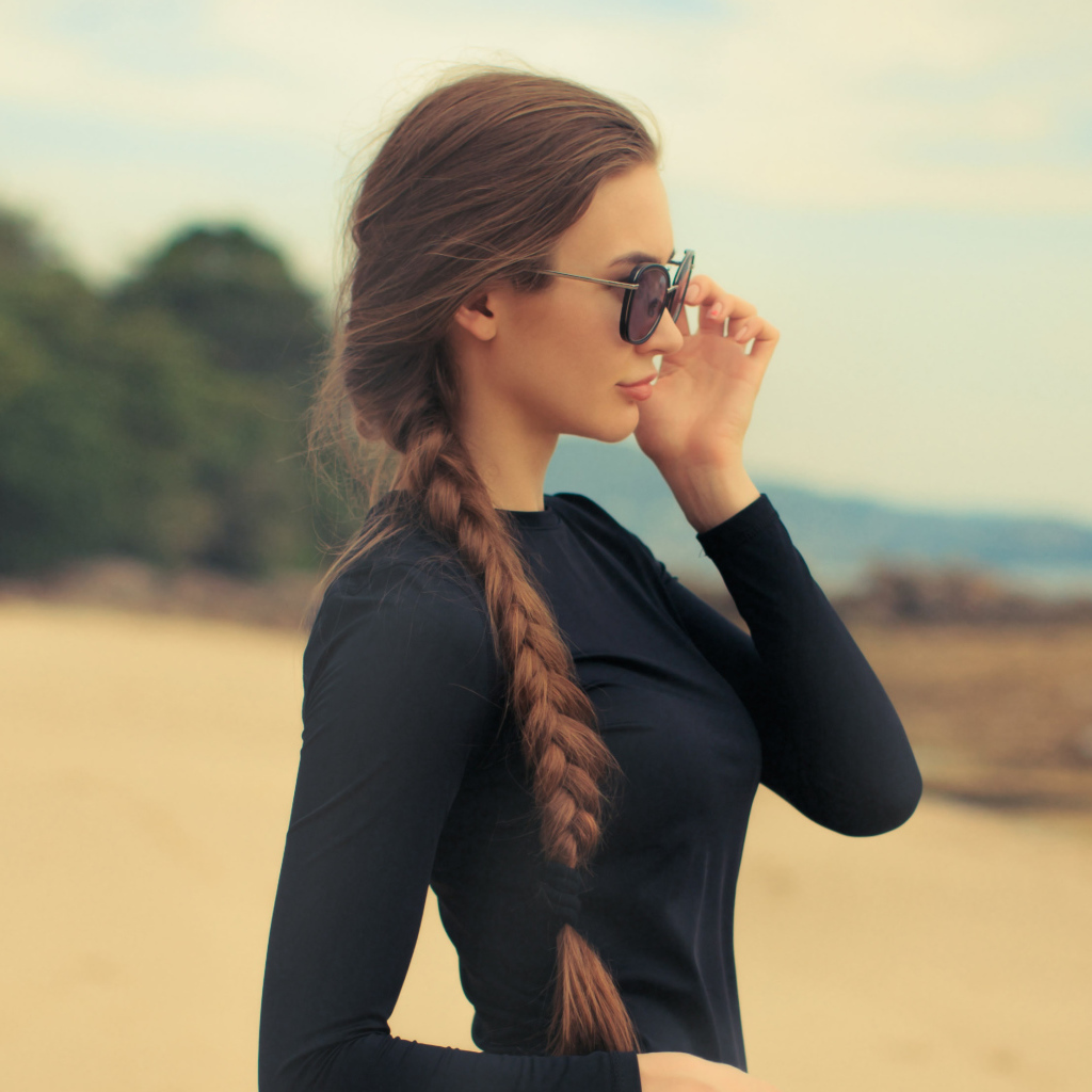 Девушка с косой в черных очках смотрит на воду