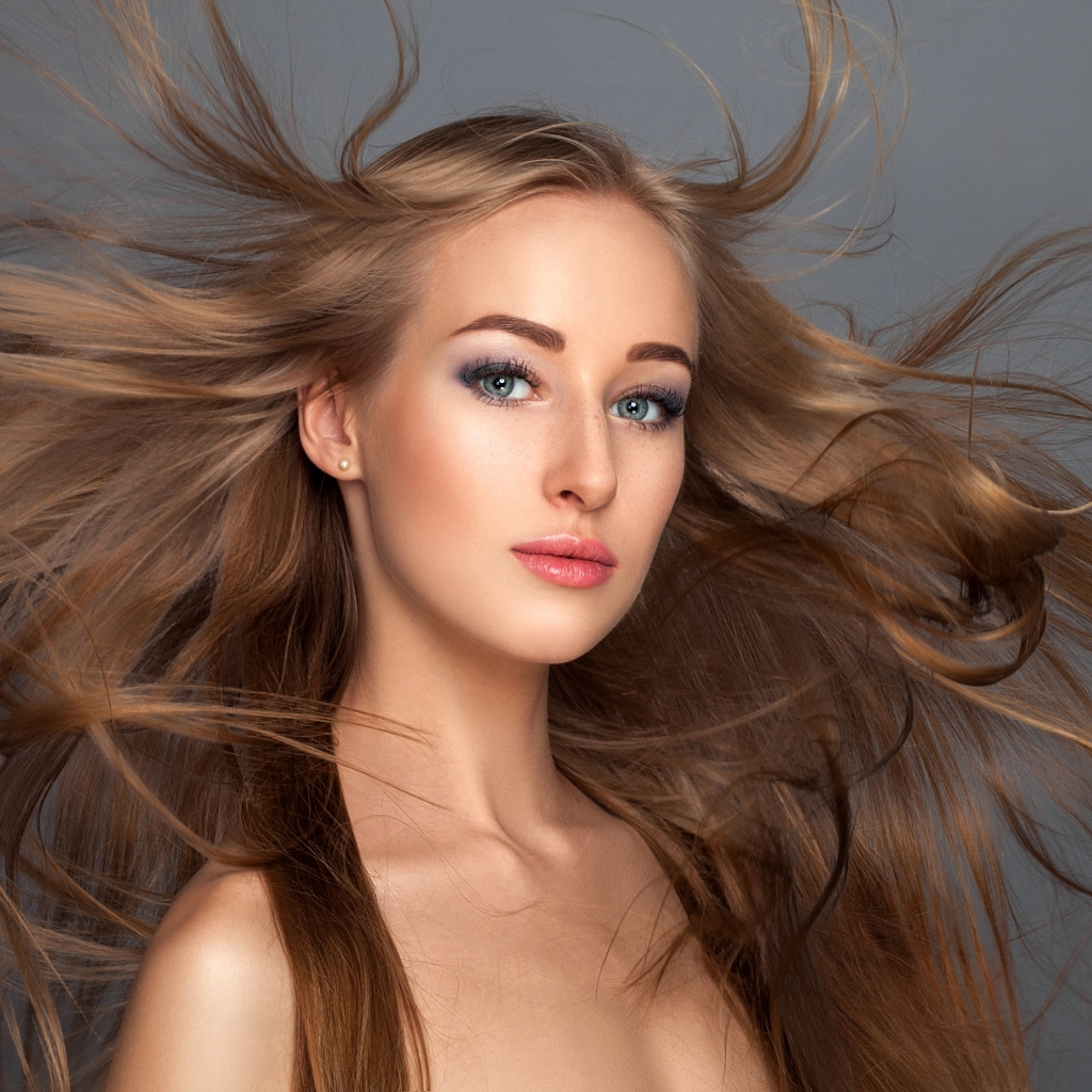 Ветер развивает волосы красивой девушке на сером фоне