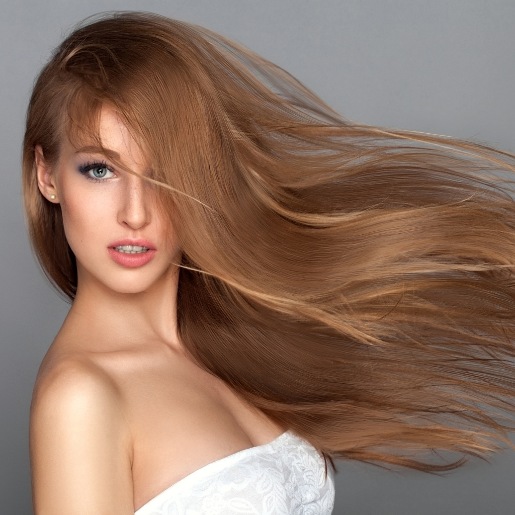 Ветер развивает волосы красивой девушки на сером фоне