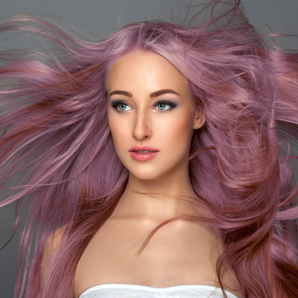 Ветер развивает розовые волосы девушки на сером фоне