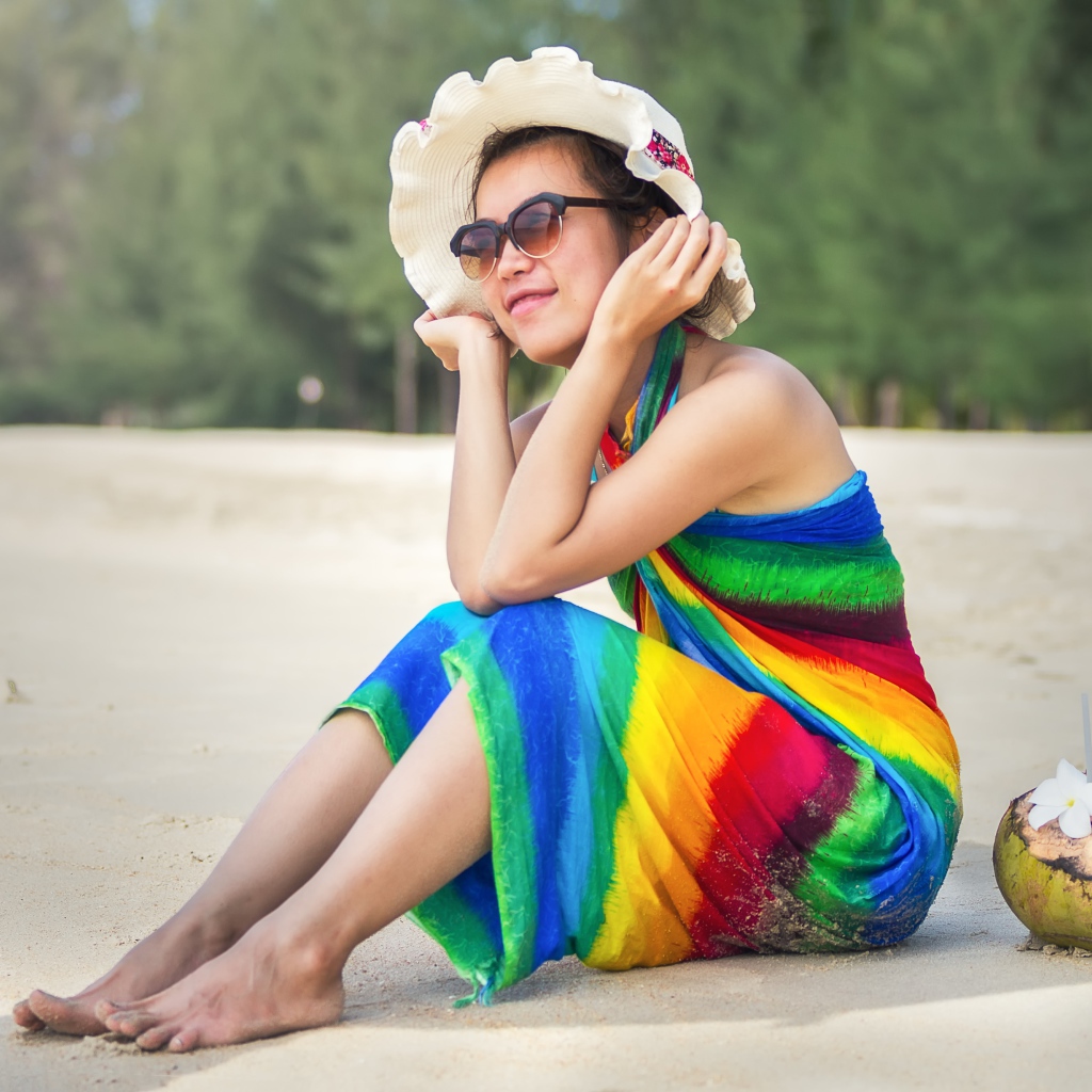 Молодая азиатка сидит на берегу с кокосом