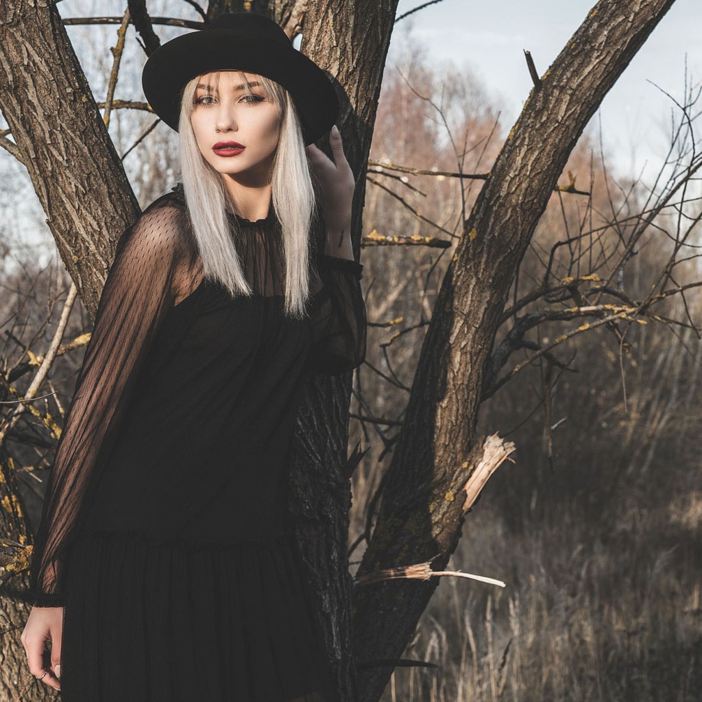 Молодая блондинка в черной шляпе у дерева