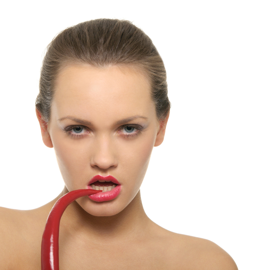 Молодая девушка кусает красный перец на белом фоне