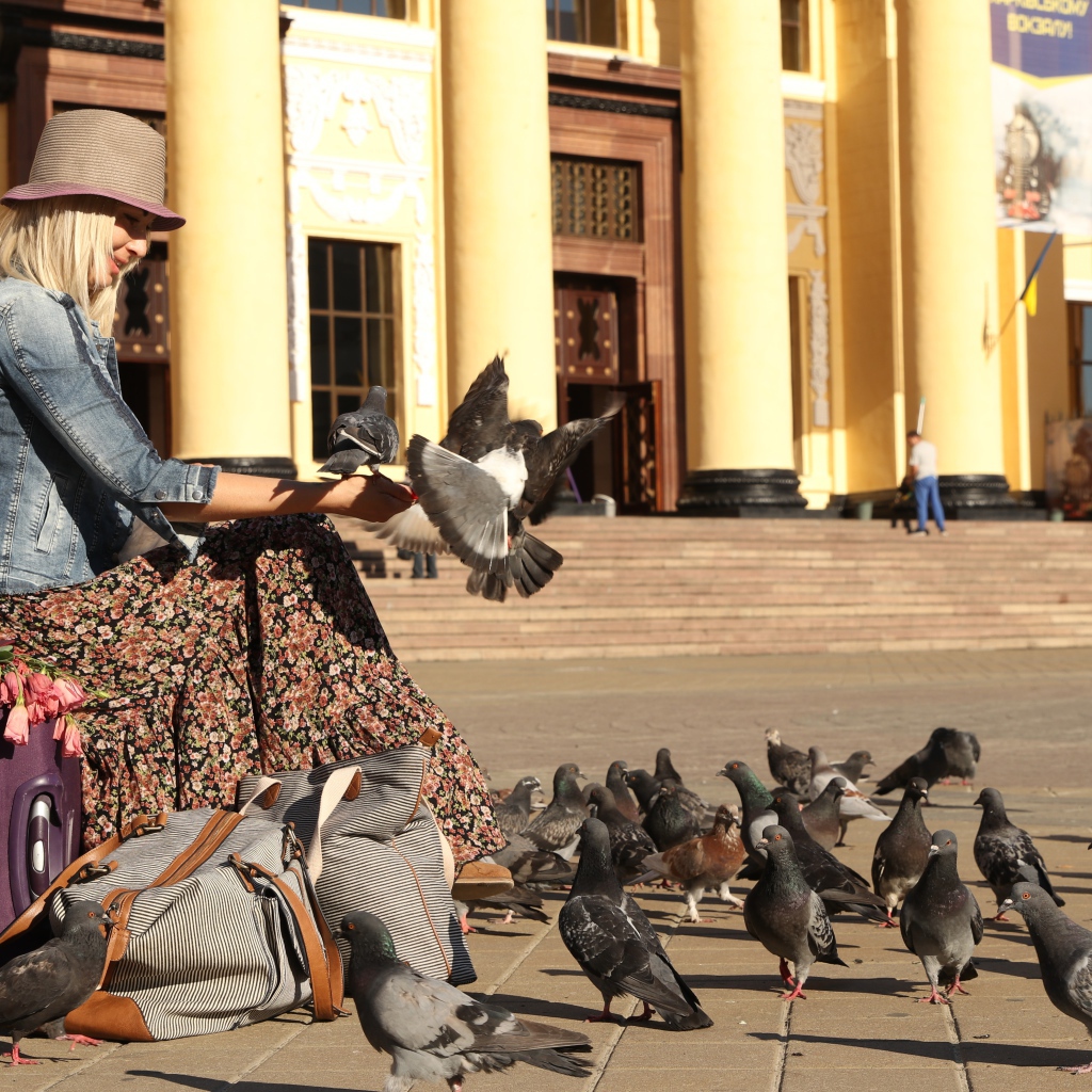 Молодая девушка кормит голубей на вокзале