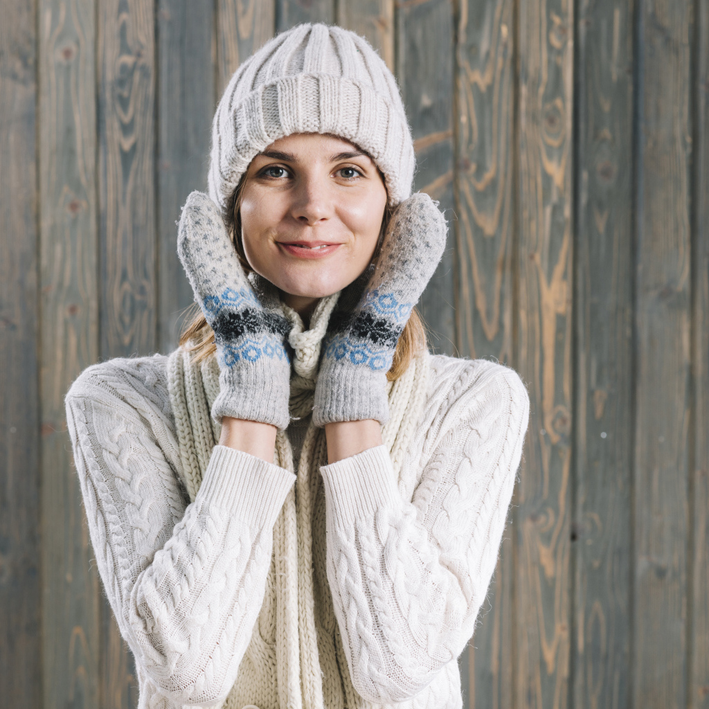 Молодая девушка на шапке, варежках  и теплой шапке на фоне забора