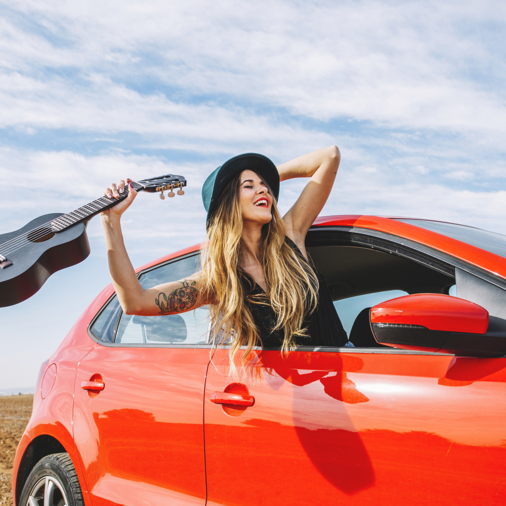 Молодая девушка с гитарой в красной машине летом