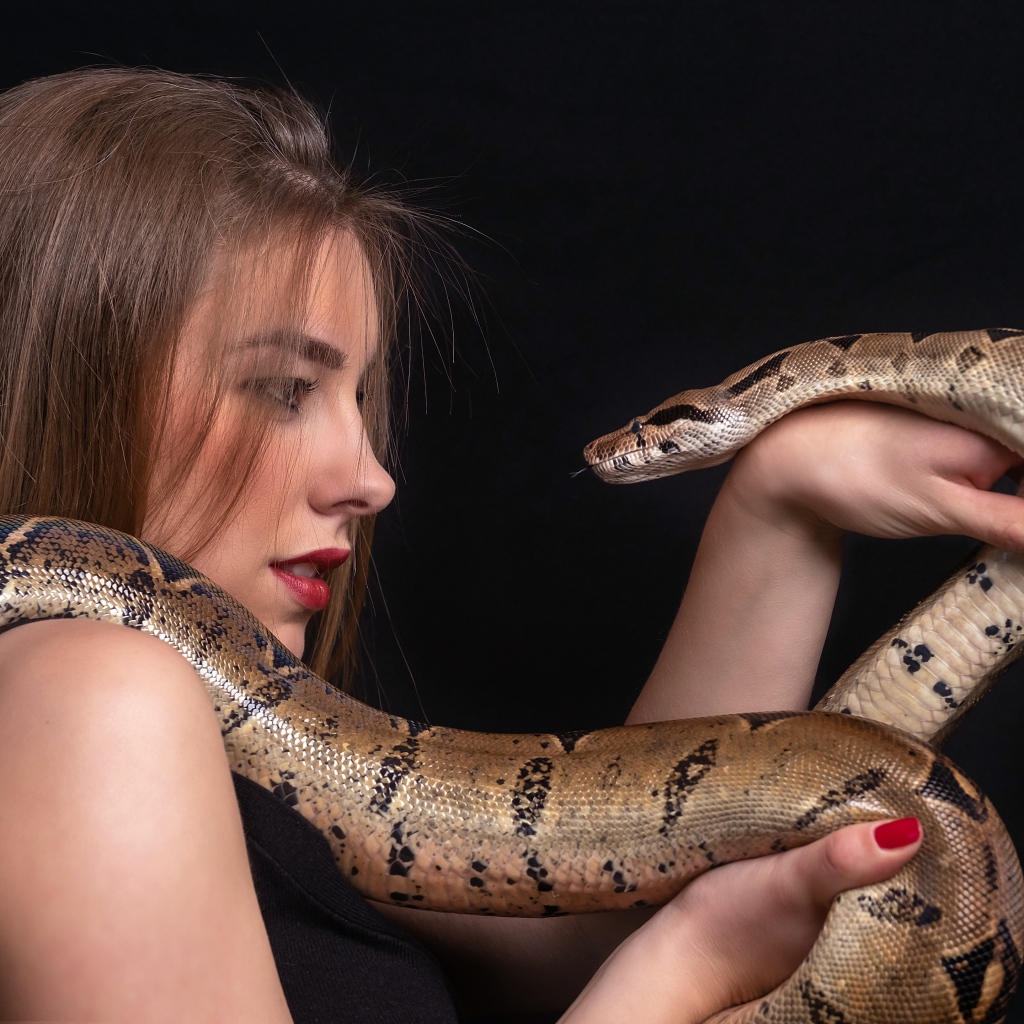 Молодая девушка со змеей в руках на черном фоне