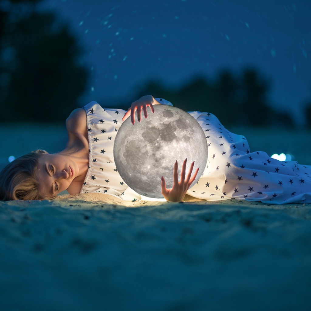 Молодая девушка с луной в руках лежит на песке