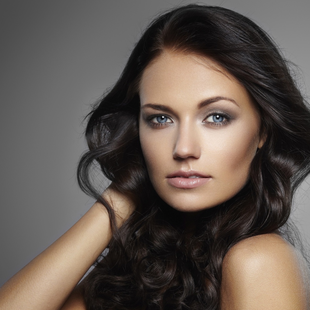 Молодая настоящая голубоглазая длинноволосая брюнетка на сером фоне