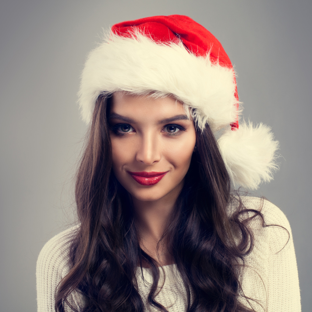 Красивая брюнетка в новогодней шапке на сером фоне