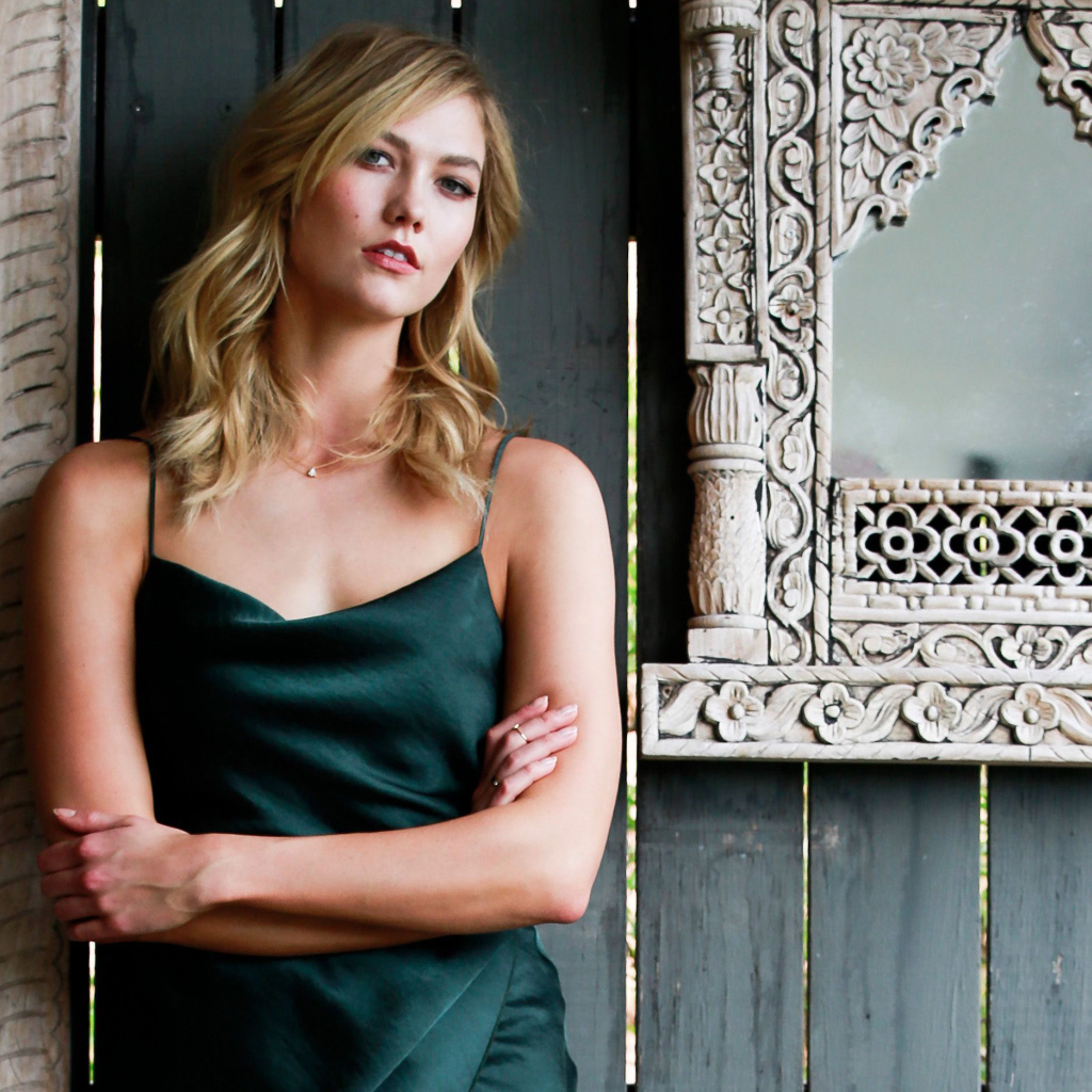 Красивая стильная модель Карли Клосс стоит у стены с зеркалом